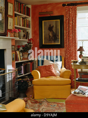 Grand tableau au-dessus de fauteuil jaune à côté de cheminée dans salon rouge avec construit dans des étagères et des rideaux rouges à motifs Banque D'Images