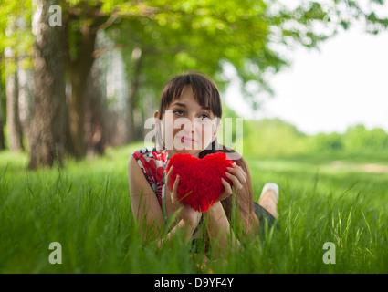 Happy girl couché dans l'herbe avec cœur dans ses mains. Banque D'Images