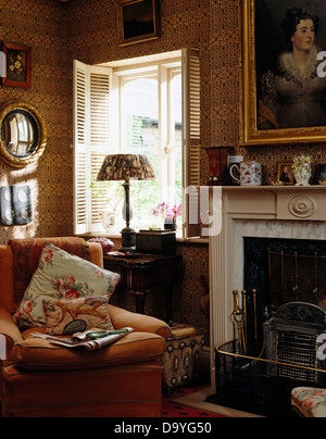 Fauteuil confortable à côté de cheminée dans salon de style victorien avec brown papier peint à motifs et des obturateurs de plantation Banque D'Images