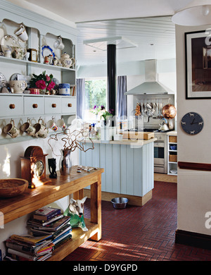 Vaisselle sur les étagères de l'armoire murale peinte au-dessus de table console simple en bois empilé avec livres en pays blanc cuisine Banque D'Images