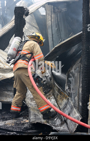 Un pompier verser de l'eau sur une structure fire hot spot Banque D'Images