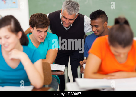 Friendly senior high school teacher helping students in classroom Banque D'Images