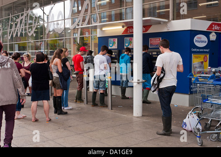 Lecture musique festivaliers attente à supermarché Tesco des distributeurs automatiques pour retirer de l'argent. Reading, Berkshire, England, GB, au Royaume-Uni. Banque D'Images