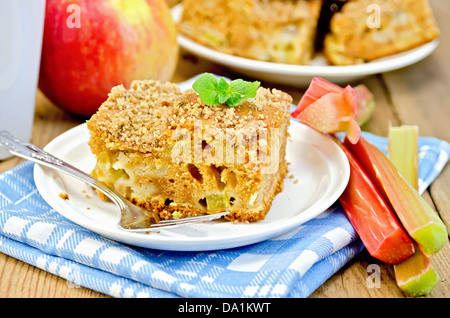 Un morceau de gâteau sucré à la rhubarbe et les pommes, menthe, bleu, serviette tasse sur l'arrière-plan de planches en bois Banque D'Images