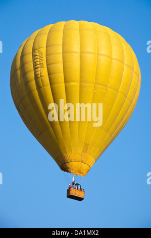 Vue verticale d'un ballon à air chaud jaune en vol avec passagers contre un ciel bleu. Banque D'Images