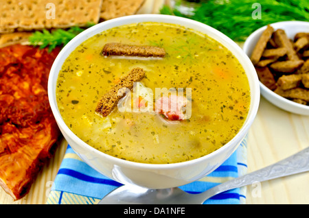 La soupe aux pois avec croûtons de seigle dans un bol et sur une assiette, une cuillère, du poivre, du pain, du tissu, du bacon, de l'aneth contre une planche en bois Banque D'Images