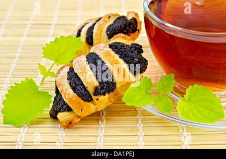 Du thé dans une tasse en verre avec deux feuilles de menthe et deux cookies pavot sur une serviette en bambou Banque D'Images