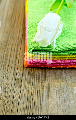 Une pile de serviettes vert, rose, orange et jaune avec tulipe blanche sur une vieille planche de bois Banque D'Images
