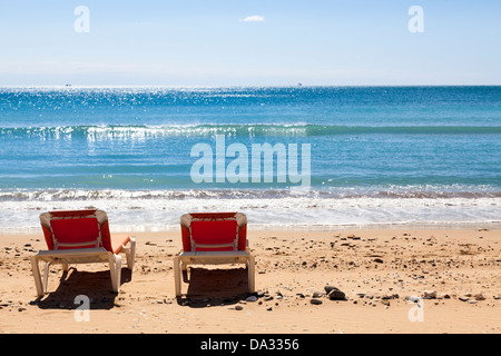 Deux chaises longues rouge inoccupées sur la plage par la mer. Banque D'Images