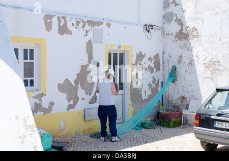 Un pêcheur réparant ses filets dans le village de pêcheurs de Ferragudo dans l'Algarve Banque D'Images