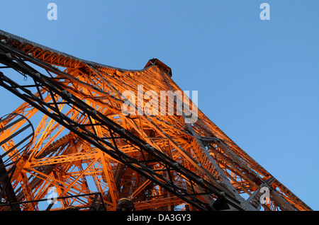 Une vue regardant vers le haut sur le tiers supérieur de la Tour Eiffel au coucher du soleil, avec les lumières faisant briller le treillis orange Banque D'Images