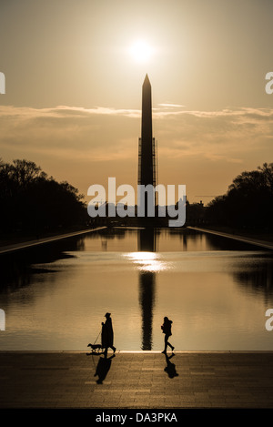 Les piétons avec leurs ombres comme le soleil matinal silhouettes le Washington Monument sur le miroir d'eau à Washington DC. Échafaudage entoure le monument partie de la montée. Banque D'Images