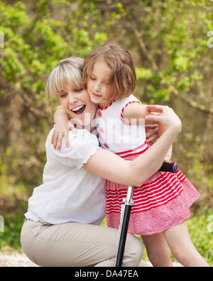 Mère et fille hug en parc avec scooter Mère et fille hug en parc avec scooter