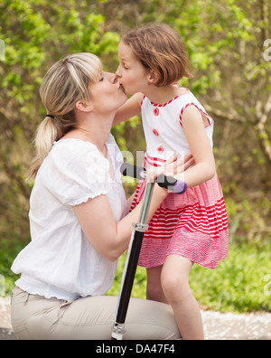 Mère et fille kissing in park with scooter Banque D'Images