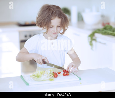 Hacher les tomates et jeune fille faisant une salade dans la cuisine Banque D'Images