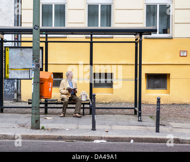 Senior man in yellow jacket livre se lit à l'arrêt de bus avec mur jaune en arrière-plan, Mitte, Berlin Banque D'Images