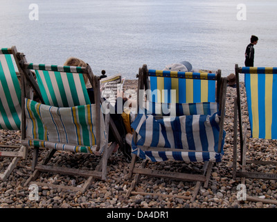 Couple assis dans des chaises longues sur la plage de lire les journaux, de la bière, Seaton, UK 2013 Banque D'Images