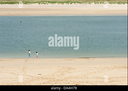 Personnes marchant sur une plage tranquille sur le fleuve de l'estuaire de Camel Padstow Cornwall UK à vers Daymer Bay et Polzeath Banque D'Images