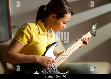 Belle Mid adult woman playing electric guitar à la maison, assis sur le canapé Banque D'Images