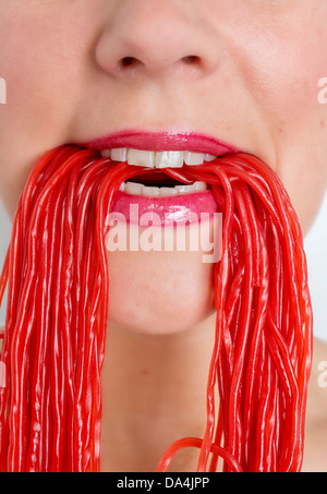 Un gros plan d'une bouche de femme de manger beaucoup de bonbons réglisse rouge dentelle Banque D'Images