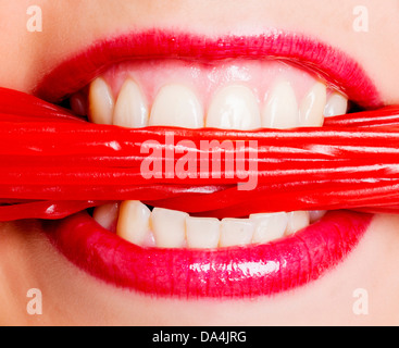 Un gros plan d'une bouche de femme de manger beaucoup de bonbons réglisse rouge dentelle Banque D'Images