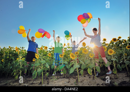 Heureux les enfants avec des ballons colorés qui saute dans un champ de tournesols Banque D'Images