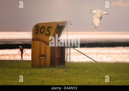 Une mouette vole passé une chaise de plage sur la mer du Nord. Banque D'Images