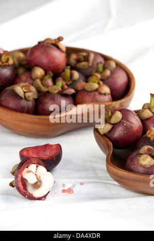 Bols de légumes marron foncé/violet mangoustan fruits sur une surface blanche. Banque D'Images