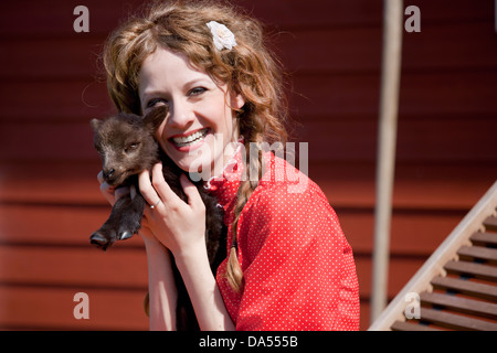 Peu d'agneau marron est prise par un bras de la jeune fille, le mouton noir, rire avec robe rouge Banque D'Images