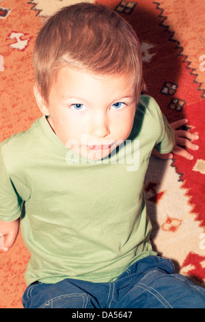 Portrait of boy (4-5) sitting on carpet, France. Banque D'Images