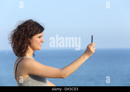 Femme faisant une photo avec un téléphone mobile avec la mer en arrière-plan Banque D'Images