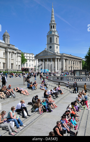 Londres, Angleterre, Royaume-Uni. Trafalgar Square. Les gens se détendre sur les étapes sur une chaude journée de printemps. L'église de St Martin in the Fields Banque D'Images