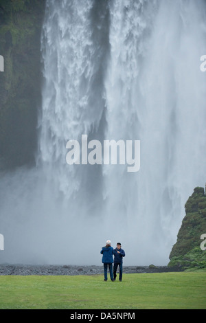 Homme conversant sur avant de Skógafoss chute sur la rivière Skoga le sud de l'Islande Europe Océan Atlantique Banque D'Images