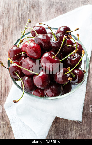 Cerises fraîches dans bol en verre sur fond de bois, selective focus Banque D'Images