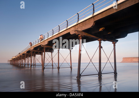 L'été bleu ciel du soir & Avis de gens debout et marcher dans le soleil, sur la jetée en bord de mer pittoresque historique sur mer calme - Sawai madhopur, England, UK. Banque D'Images