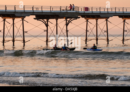 Ciel coucher de soleil d'été colorés et voir des gens marcher sur la jetée en bord de mer et 3 hommes en kayak Kayak de mer en mer par - Sawai madhopur, England, UK Banque D'Images