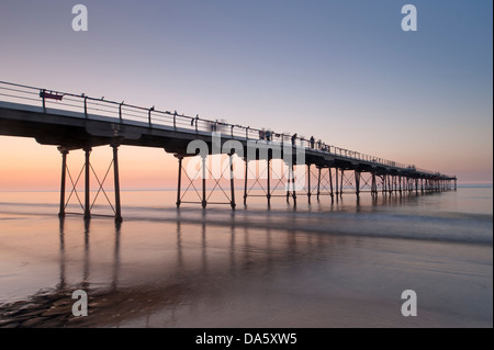 En vertu de l'été haut en couleurs, de ciel coucher de soleil Vue de la plage de sable de personnes marchant sur la jetée en bord de mer historique sur mer calme - Sawai madhopur, England, UK. Banque D'Images