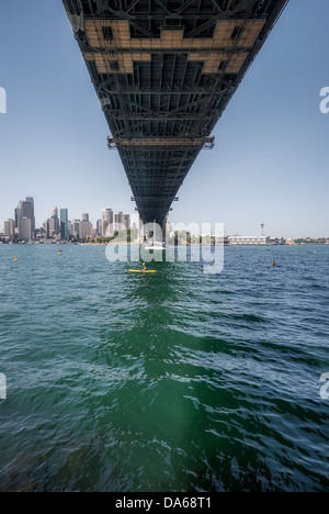 Une vue unique d'un voilier surpassé par le sous-ventre de l'emblématique Sydney Harbour Bridge qui s'étend du centre-ville au nord de Sydney. Banque D'Images