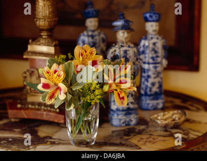 Close-up of small posy de alstromeria en vase en verre recouvert de marbre fleurs sur table avec figurines chinois blanc +bleu Banque D'Images