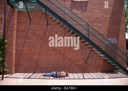 13 juin 2013 - Flagstaff, Arizona, États-Unis - un sans-abri dort sur la rue à proximité d'un escalier et mur de pierre. Flagstaff est situé à proximité de Mont Elden, juste au sud de la San Francisco Peaks, près de la limite sud-ouest du Plateau du Colorado. Flagstaff dispose d'un secteur touristique fort, en raison de sa proximité avec le Parc National du Grand Canyon, Oak Creek Canyon, l'Arizona Snowbowl, Meteor Crater, et l'historique Route 66. Flagstaff a acquis une réputation comme un aimant pour les amateurs de plein air, et la diversité de son relief, l'altitude élevée, et peut faire l'attirer les campeurs, randonneurs météo, grimpeurs, Banque D'Images