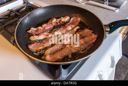 Bacon à la poêle dans un poêlon, sur fond blanc cuisinière dans une cuisine. USA. Banque D'Images