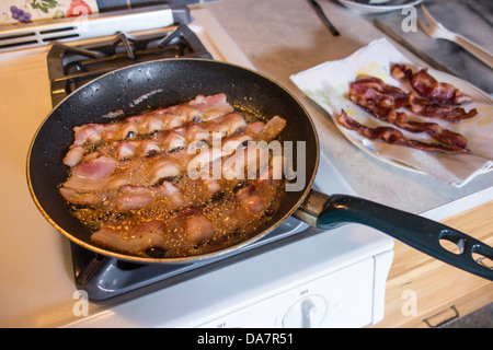 Faire frire le bacon dans une poêle sur une cuisinière blanche dans une cuisine américaine. USA. Banque D'Images