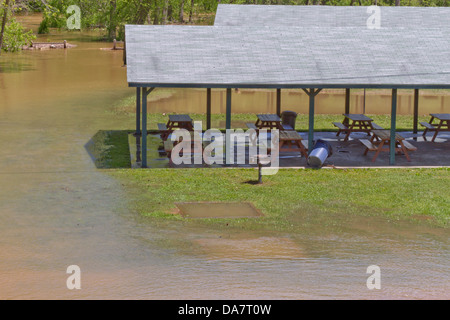 Une rivière inondations un couverts de pique-nique avec bancs dans un parc Banque D'Images