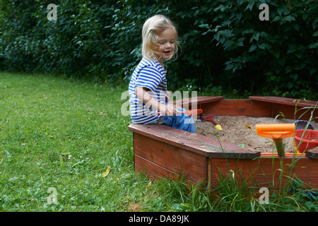 Enfant fille blonde jouant avec le sable sur l'aire de jeux Banque D'Images