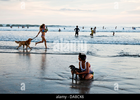 Femme en marche avec un chien sur la plage de Kuta est regardé par une femme se baigner son chien Banque D'Images