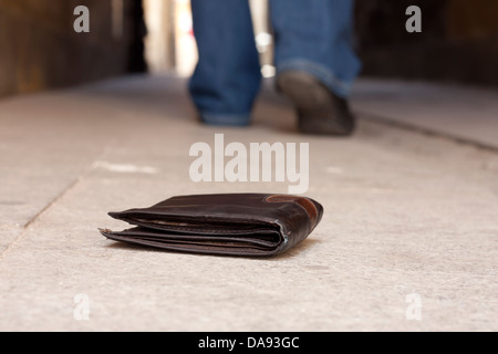 Portefeuille perdu dans la rue et les jambes de l'homme marche concept Banque D'Images