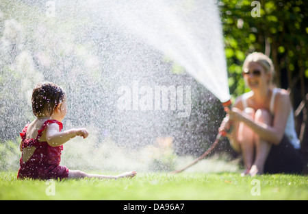 Un bébé crie de plaisir alors qu'elle est refroidie par mom pulvériser de l'eau d'un tuyau de jardin. Banque D'Images