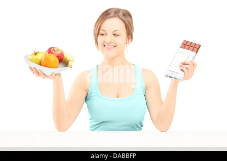 Jeune femme tenant une corbeille de fruits frais et le chocolat, essayant de décider lequel de manger Banque D'Images