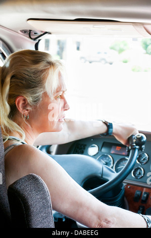 Femme blonde en conversation sur le téléphone cellulaire en conduisant un gros camion. Banque D'Images