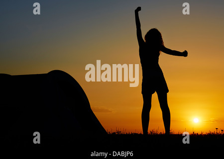 Silhouette d'une femme debout et reposant près d'une tente de camping au lever du soleil. Banque D'Images